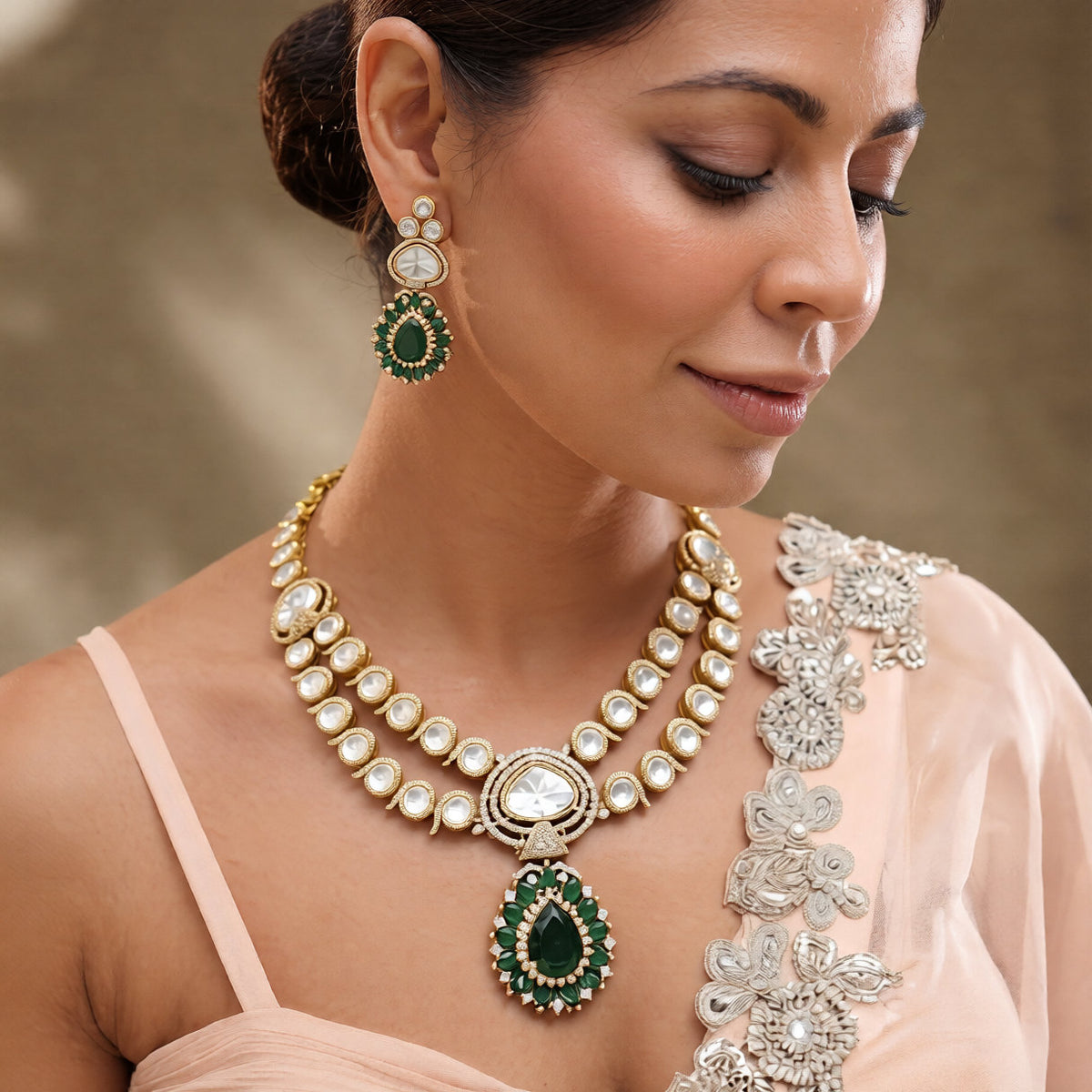 Antique gold two-strand polki kundan necklace with emerald green teardrop pendant on a display bust