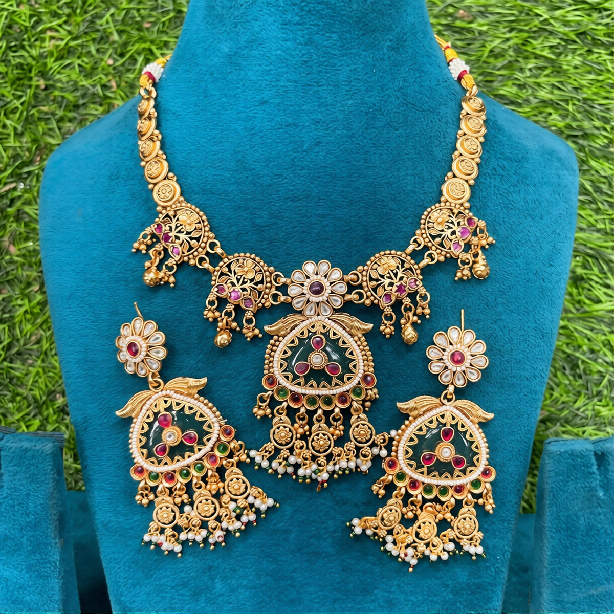Antique matte gold temple necklace set with green triangular pendant, ruby pink stones, pearl drops and matching chandelier earrings on teal bust