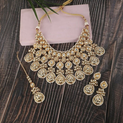 Gold-toned bridal kundan necklace set with pearl edging, maang tikka, and matching jhumka earrings