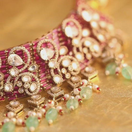 Kundan bridal necklace set with pink stones, green bead drops, and matching statement earrings in gold tone

