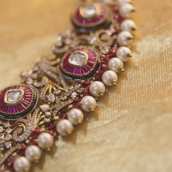 Gold-tone traditional necklace set with pink kundan-style stones, intricate detailing, pearl bead drops, and matching ornate dangling earrings.