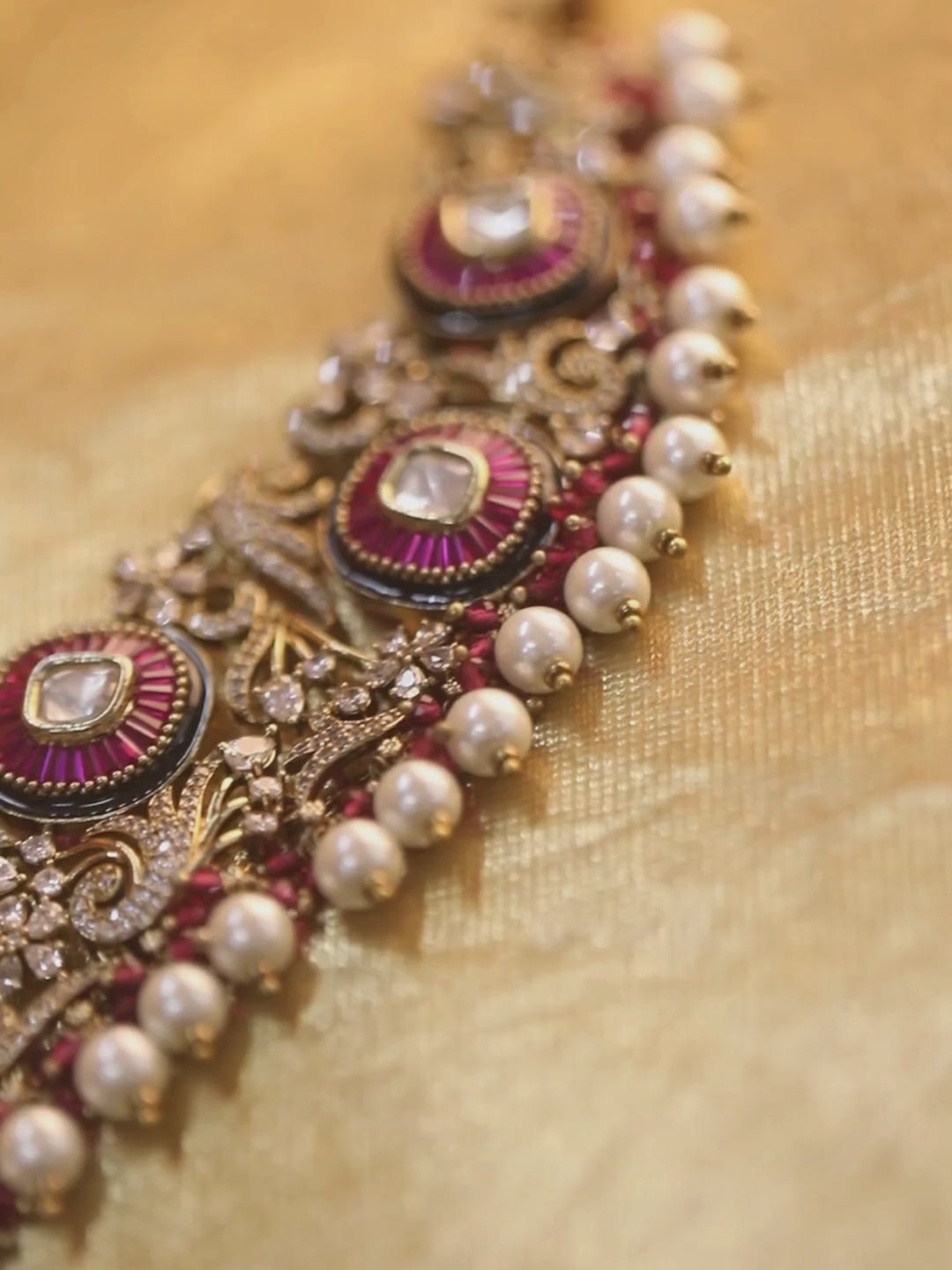 Gold-tone traditional necklace set with pink kundan-style stones, intricate detailing, pearl bead drops, and matching ornate dangling earrings.