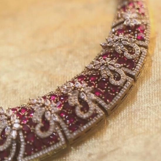 Gold-tone statement necklace set with pink ruby-style stones and clear crystals in an intricate floral design, paired with matching chandelier earrings featuring drop accents.