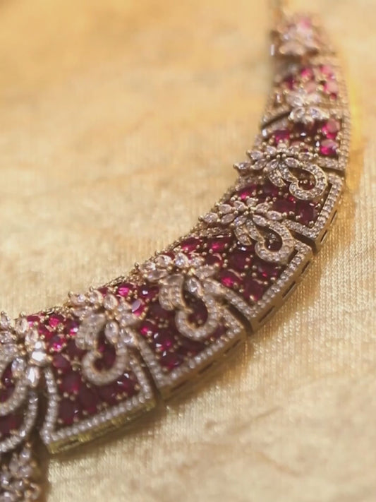 Gold-tone statement necklace set with pink ruby-style stones and clear crystals in an intricate floral design, paired with matching chandelier earrings featuring drop accents.