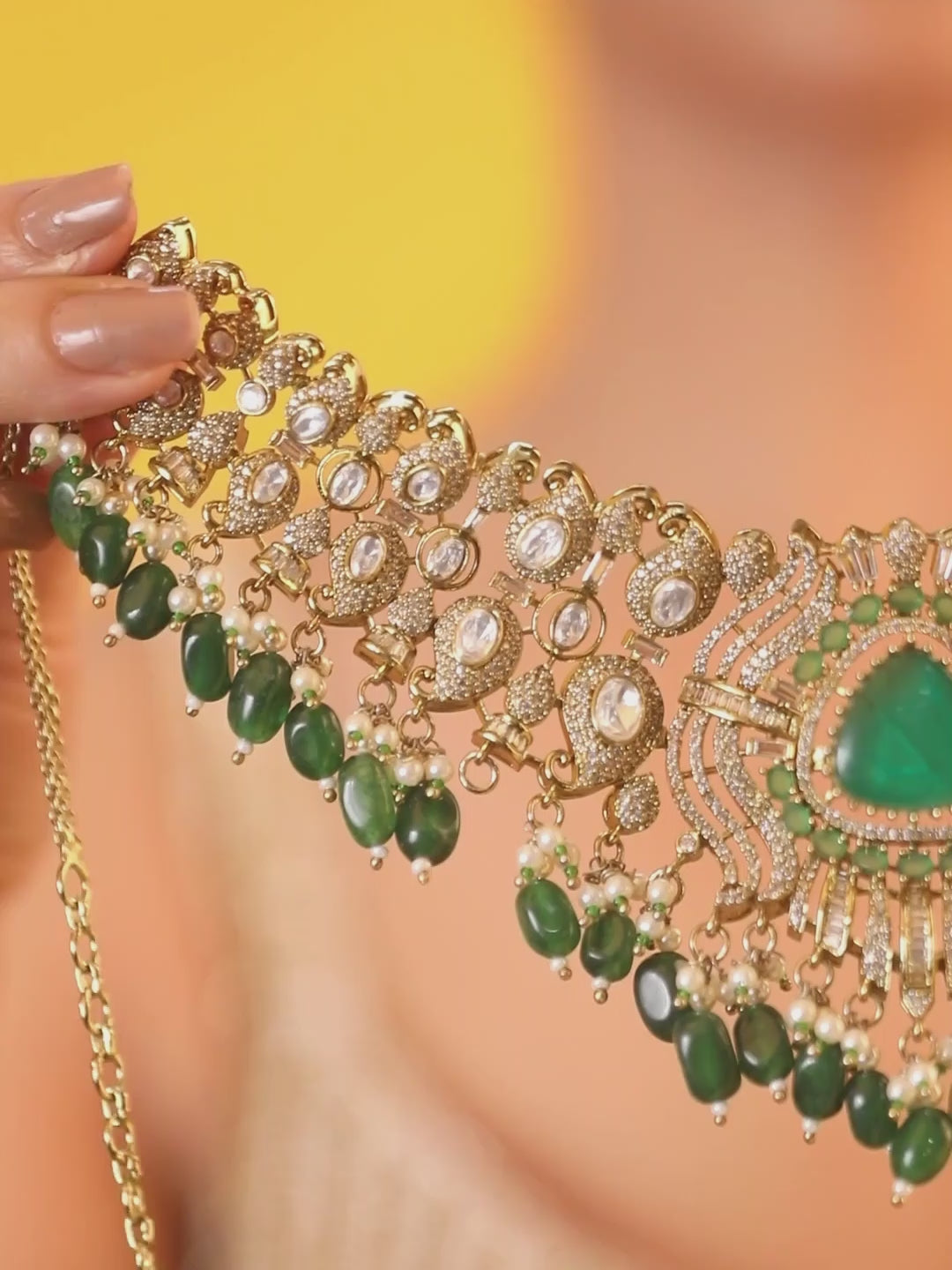 Detailed gold-toned statement necklace with intricate white stone embellishments and a prominent green teardrop centerpiece, finished with dangling green beads and pearls, paired with matching ornate drop earrings, displayed on a plain light background.