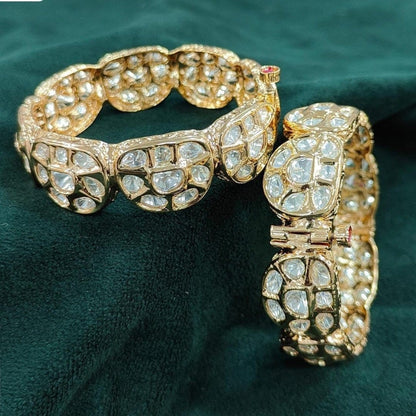 Traditional Gold Plated Kundan Bangles with Polki Stone Embellishment - Auraa Trends - Bangles -  - Auraa Trends - Gold plated traditional polki kundan bangles with petal - shaped panels, perfect for bridal and festive wear – displayed on a textured stone background with floral decor
