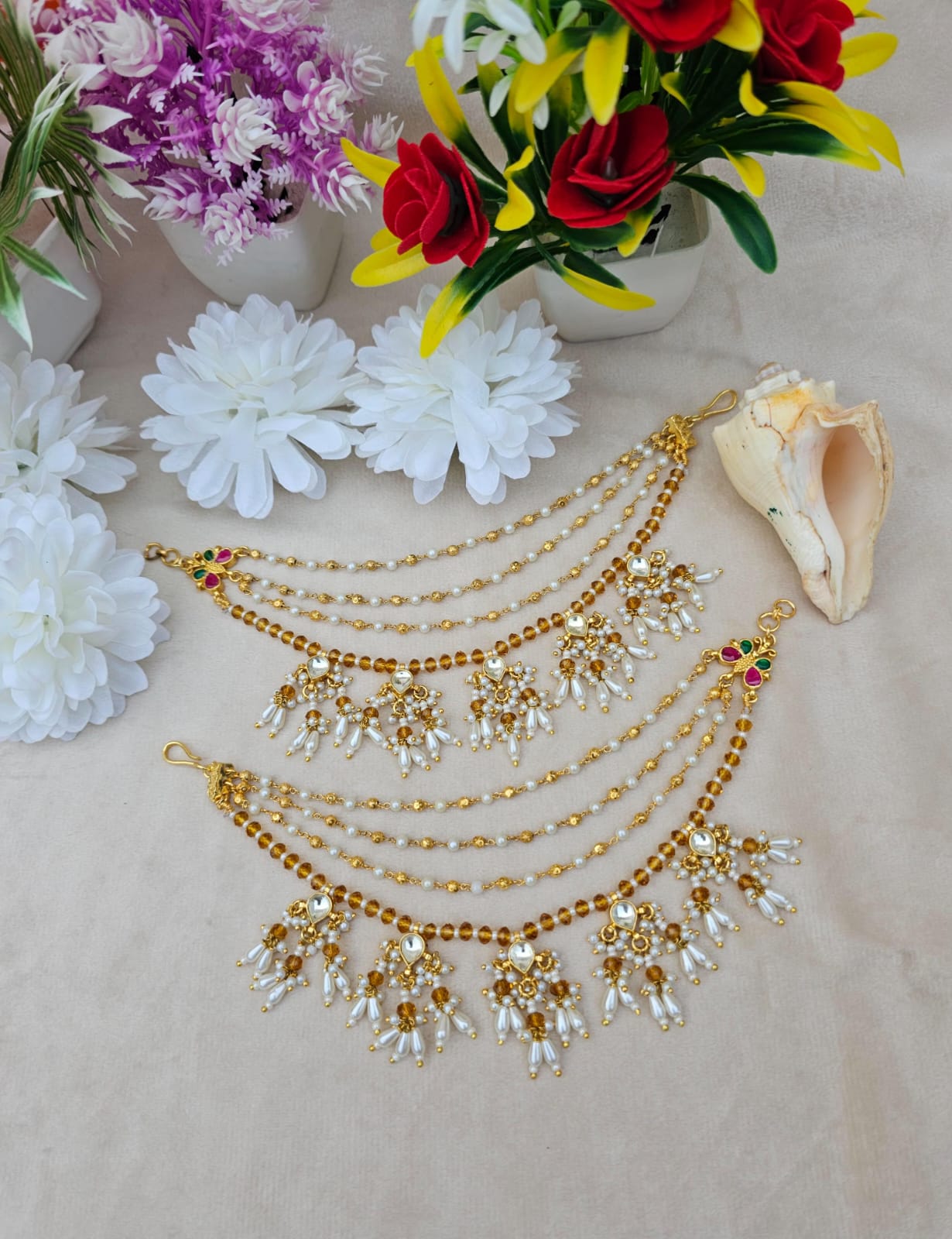Traditional Kundan & Pearl Multi - Layer Kaan Chain - Auraa Trends - Kaan chain -  - Auraa Trends - Elegant multi - layered Kundan and pearl golden Kaan Chain (Ear Chain) with floral motifs and dangling pearl drops, displayed with decorative flowers and seashell.