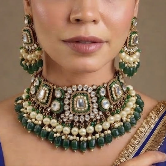 Gold kundan choker necklace set with green meenakari motifs, pearl and green bead drops and matching chandelier earrings on brown 